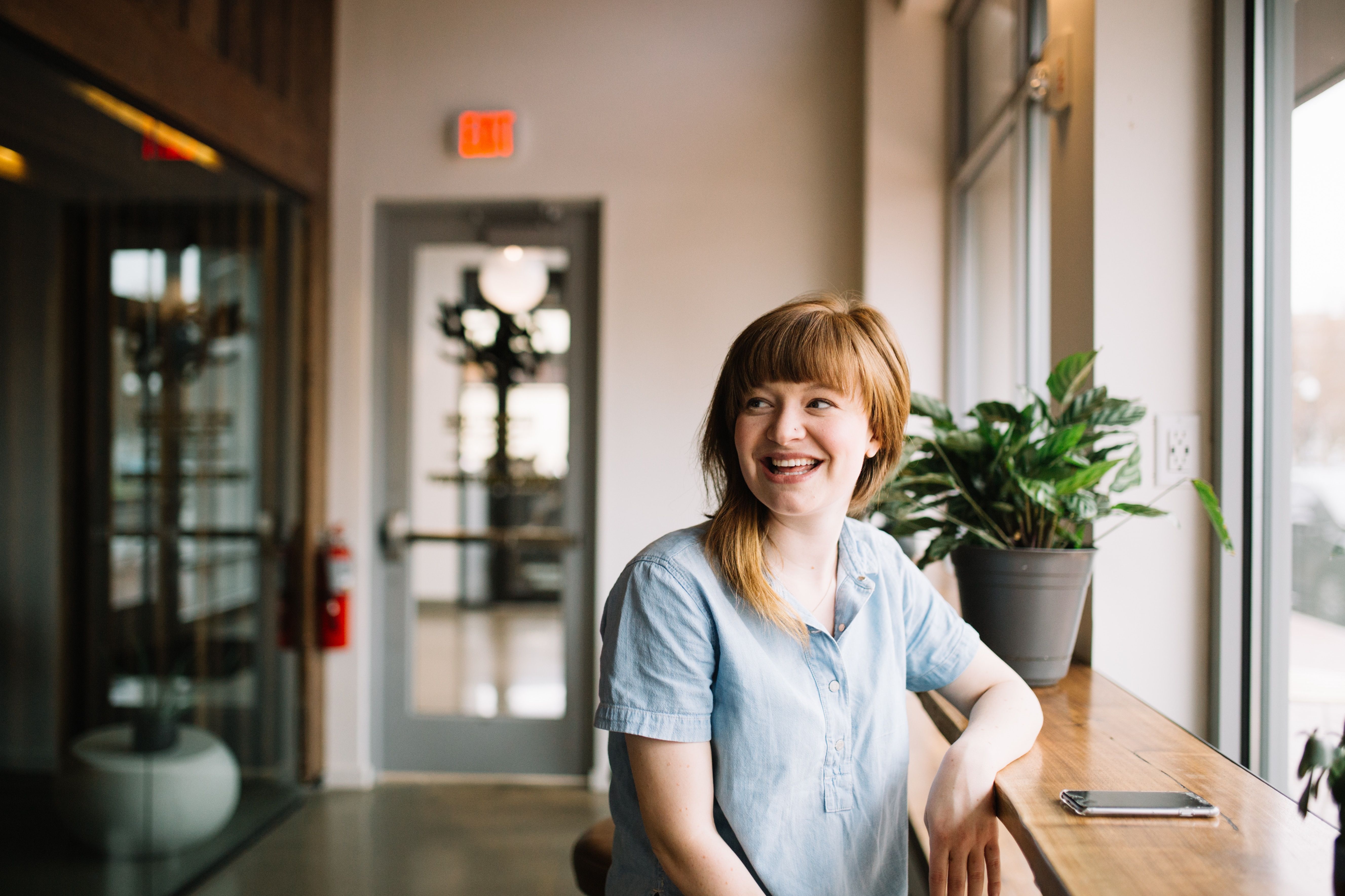 Smiling woman sitting at a window desk with her phone